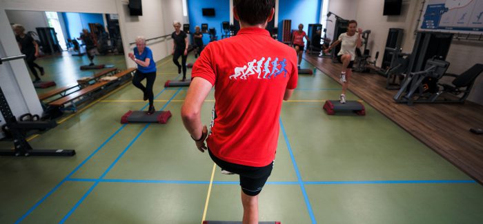 Een man geeft een steps-les in een sportstudio, waarbij deelnemers de bewegingen op de step volgen.