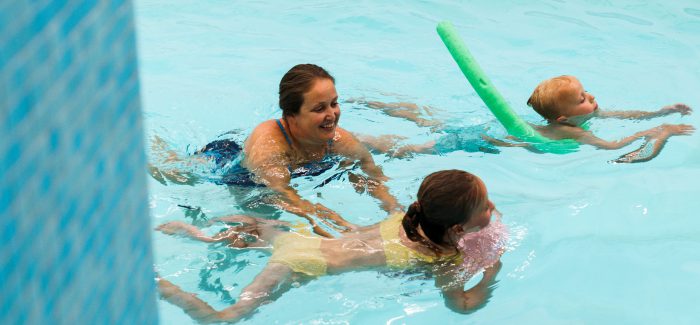Twee kinderen die met een zwemjuf aan het zwemmen zijn in een binnenzwembad