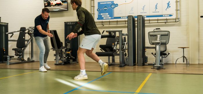 Fysiotherapeut geeft een jongen van 15 jaar instructies voor het uitvoeren van een stabiliteitsoefening gericht op landingstechniek in de oefenzaal.