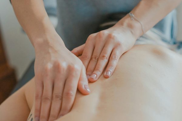 Fysiotherapeute voert een rugonderzoek uit bij een vrouw die op haar buik ligt op een behandelbank.